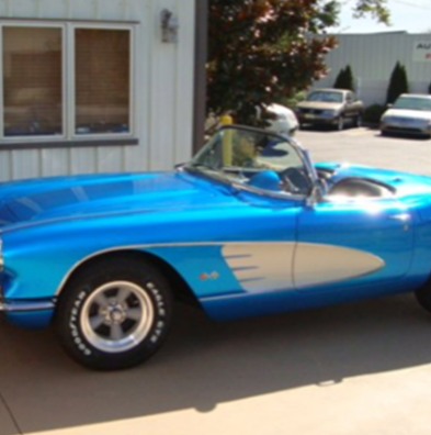 A blue car with goodyear tires is parked in front of a building