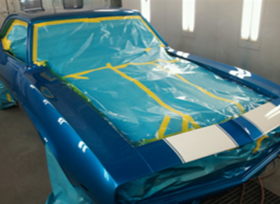A blue car is being painted in a paint booth