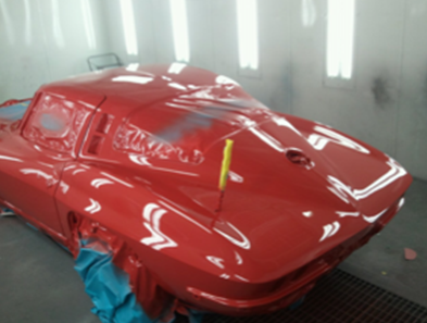 A red car is being painted in a paint booth