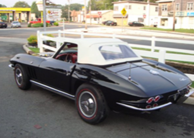 A black corvette with a white top is parked on the side of the road