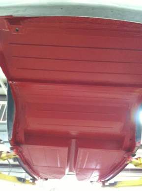 A red car is sitting on a lift in a garage.