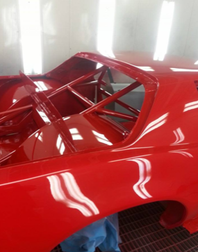 A red car is being painted in a paint booth
