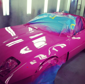 A pink car is being painted in a paint booth
