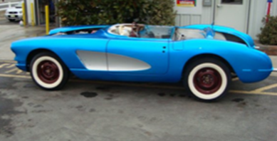 A blue car with white tires is parked in a parking lot