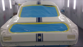 A white car is being painted in a paint booth