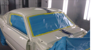 A white car is being painted in a paint booth.