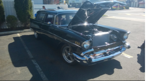 A black car with the hood up is parked in a parking lot.