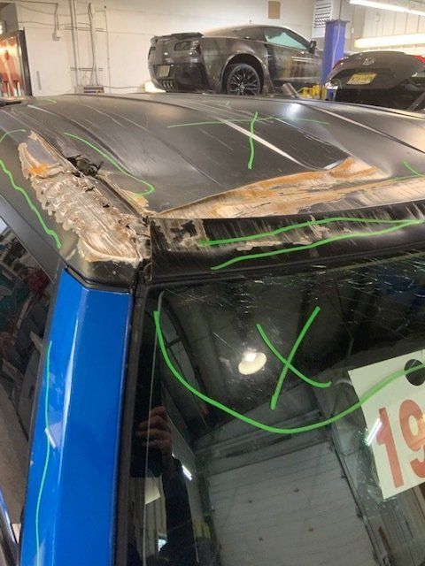 A blue car with a damaged roof is sitting in a garage.