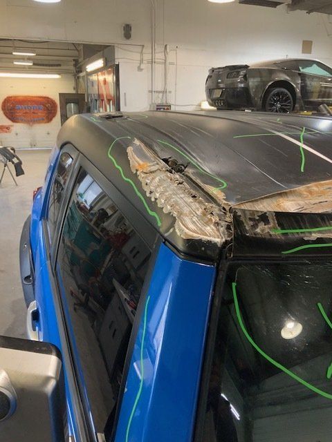 A blue car with a damaged roof in a garage
