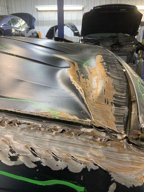 The hood of a car is being repaired in a garage.