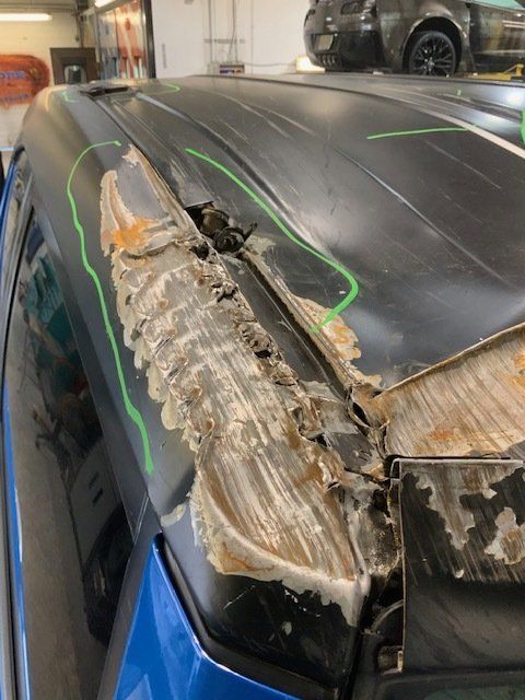 A blue car with a damaged roof is sitting in a garage.