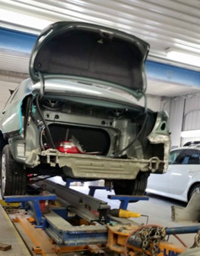 A car is being worked on in a garage with the trunk open