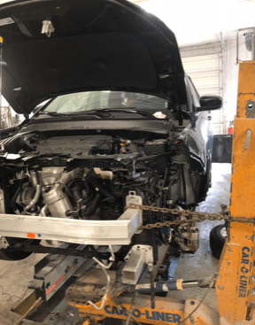 A car with the hood up is being worked on by a mechanic.
