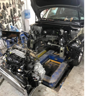 A car is being dismantled in a garage with the hood open