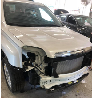A white car with a damaged front end is sitting in a garage