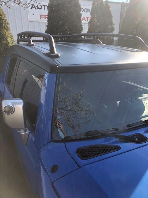 A blue suv with a black roof rack is parked in front of a building.