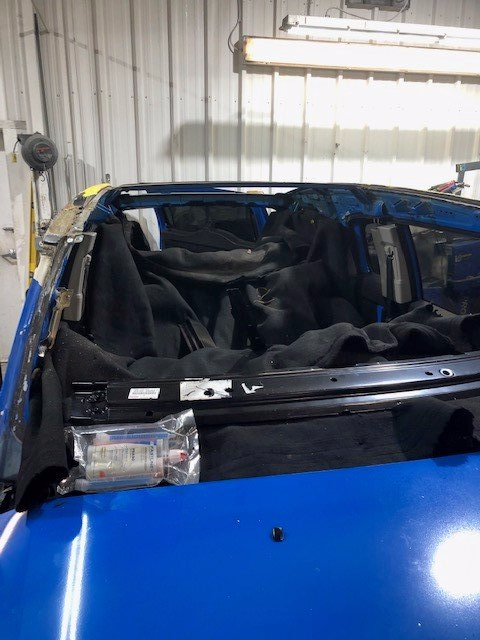 A blue car with a broken windshield is sitting in a garage.
