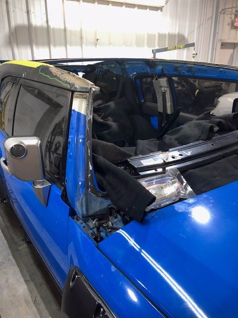 A blue car with a broken windshield is parked in a garage.