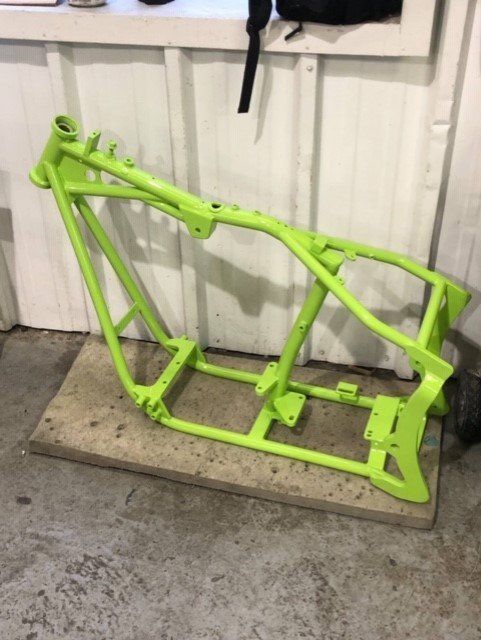 A green motorcycle frame is sitting on a concrete surface