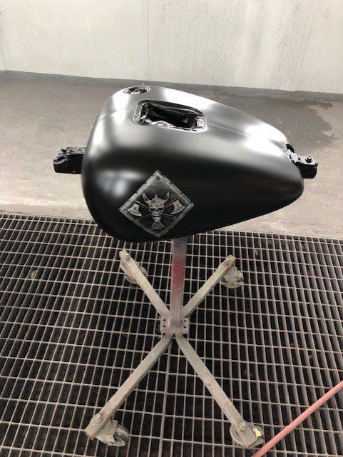 A black motorcycle tank is sitting on top of a metal stand.