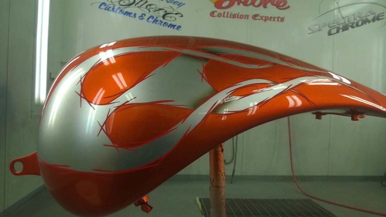 An orange and silver motorcycle tank is sitting on a table in a paint booth.