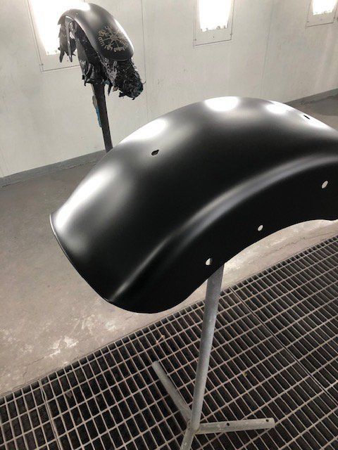 A black motorcycle fender is sitting on a metal stand