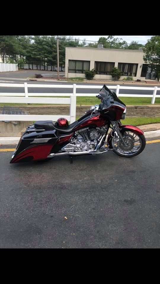 A red and black motorcycle is parked on the side of the road next to a white fence.