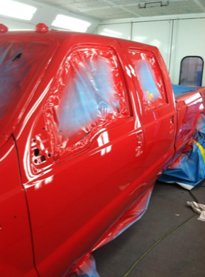 A red truck is being painted in a paint booth