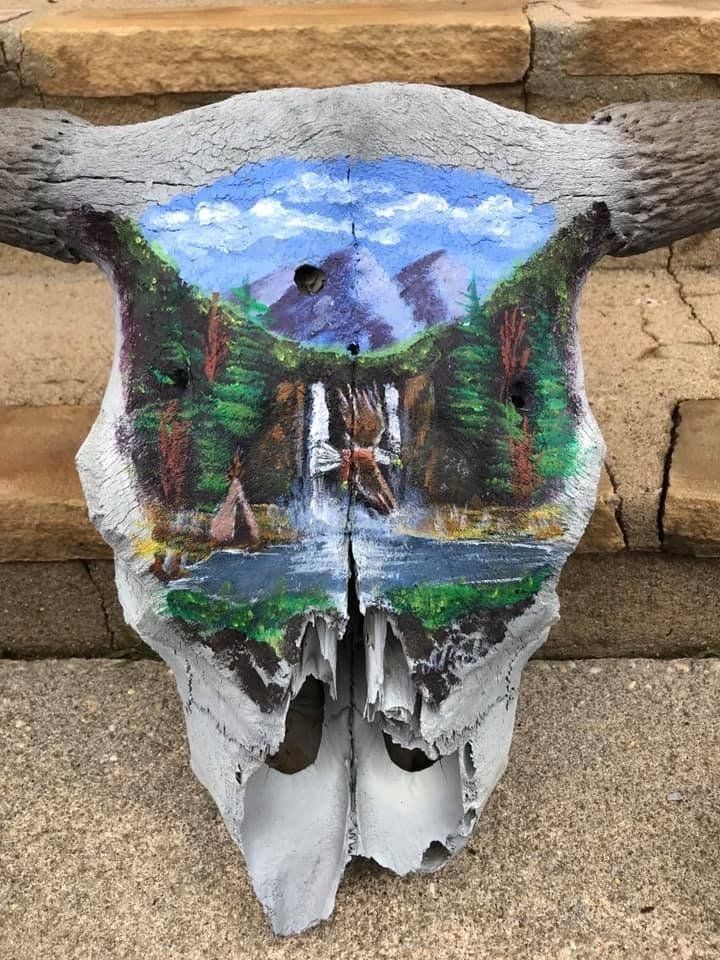 A bull skull with a painting of a waterfall on it.