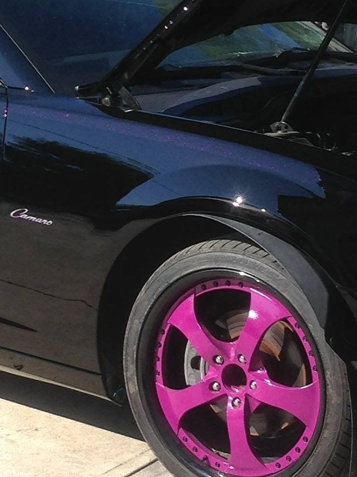 A black car with a purple wheel is parked on the sidewalk