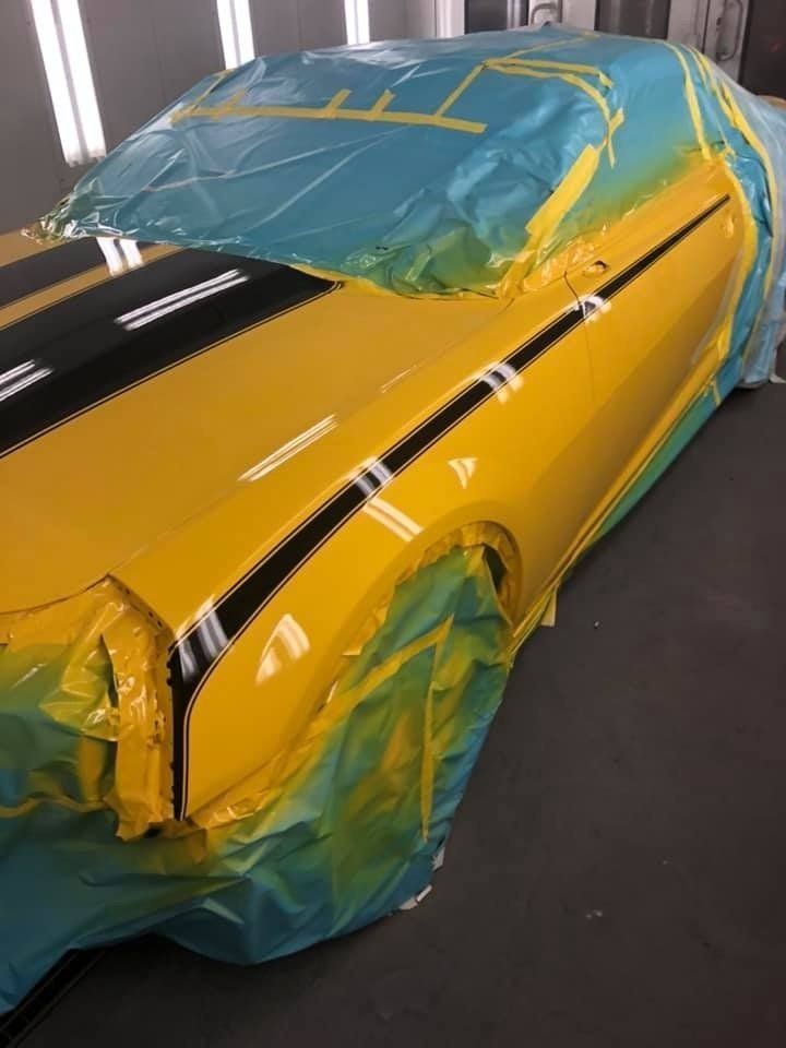A yellow car with black stripes is being painted