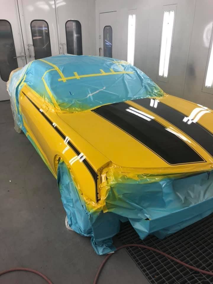 A yellow car is being painted in a paint booth