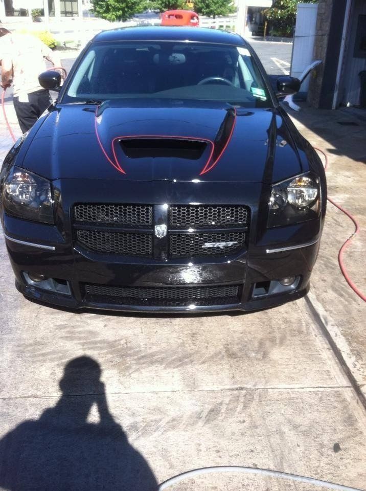 A black car with red stripes on the hood is parked on the side of the road.