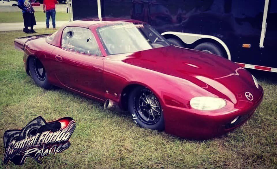A red race car is parked in the grass next to a trailer.