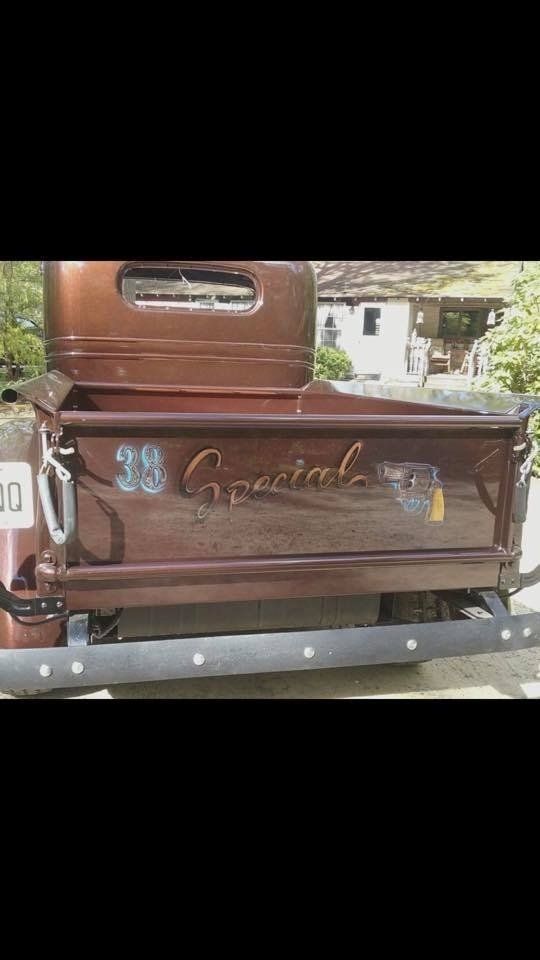 The back of a brown truck with a wooden bed is parked in front of a house.