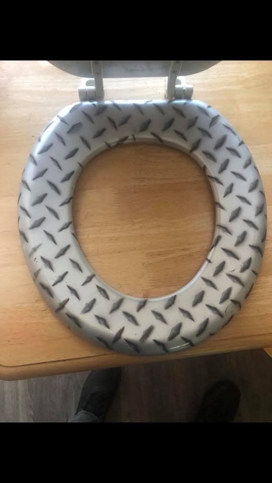 A toilet seat with a diamond plate pattern is sitting on a wooden table.