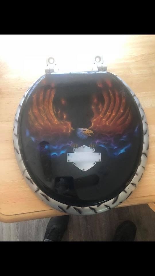 A toilet with a harley davidson logo on it is sitting on a wooden table.