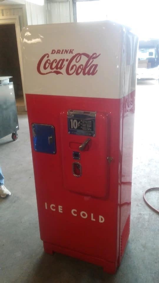 A red and white coca cola vending machine is sitting in a garage.