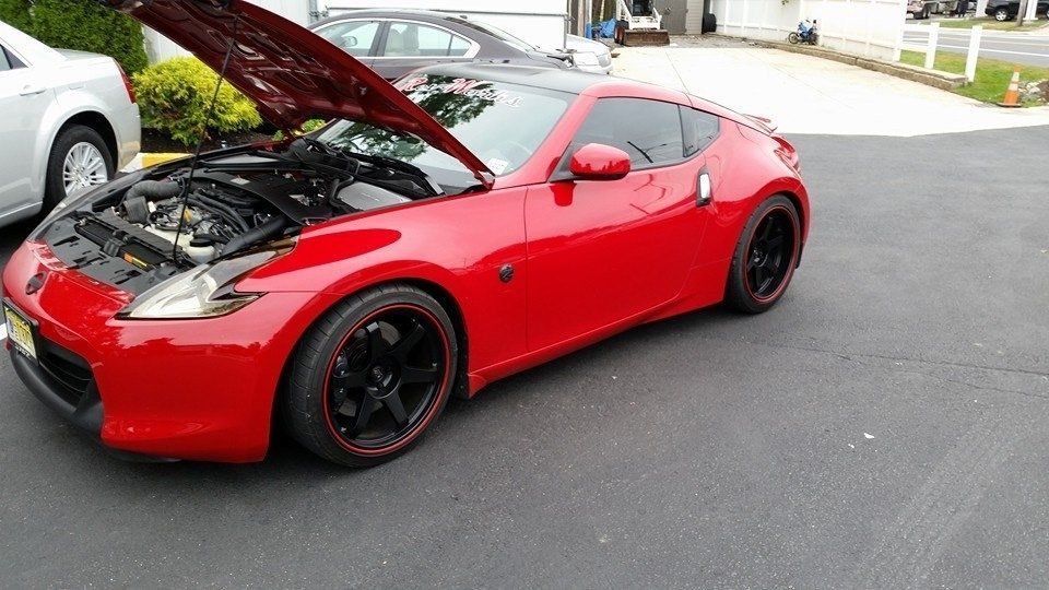 A red sports car with the hood up is parked in a driveway
