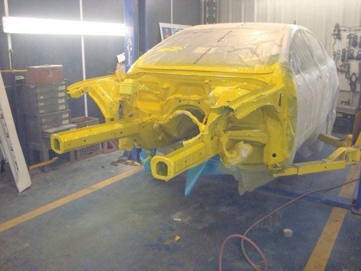 A yellow car is being painted in a garage
