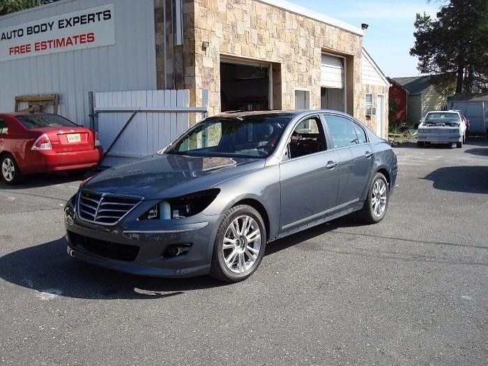 A gray car is parked in front of a building that says auto body experts