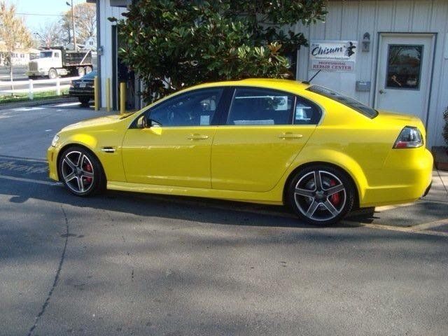 A yellow car is parked in front of a car dealership