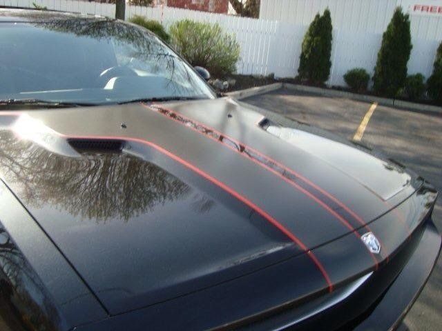 A black car with red stripes on the hood is parked in a parking lot