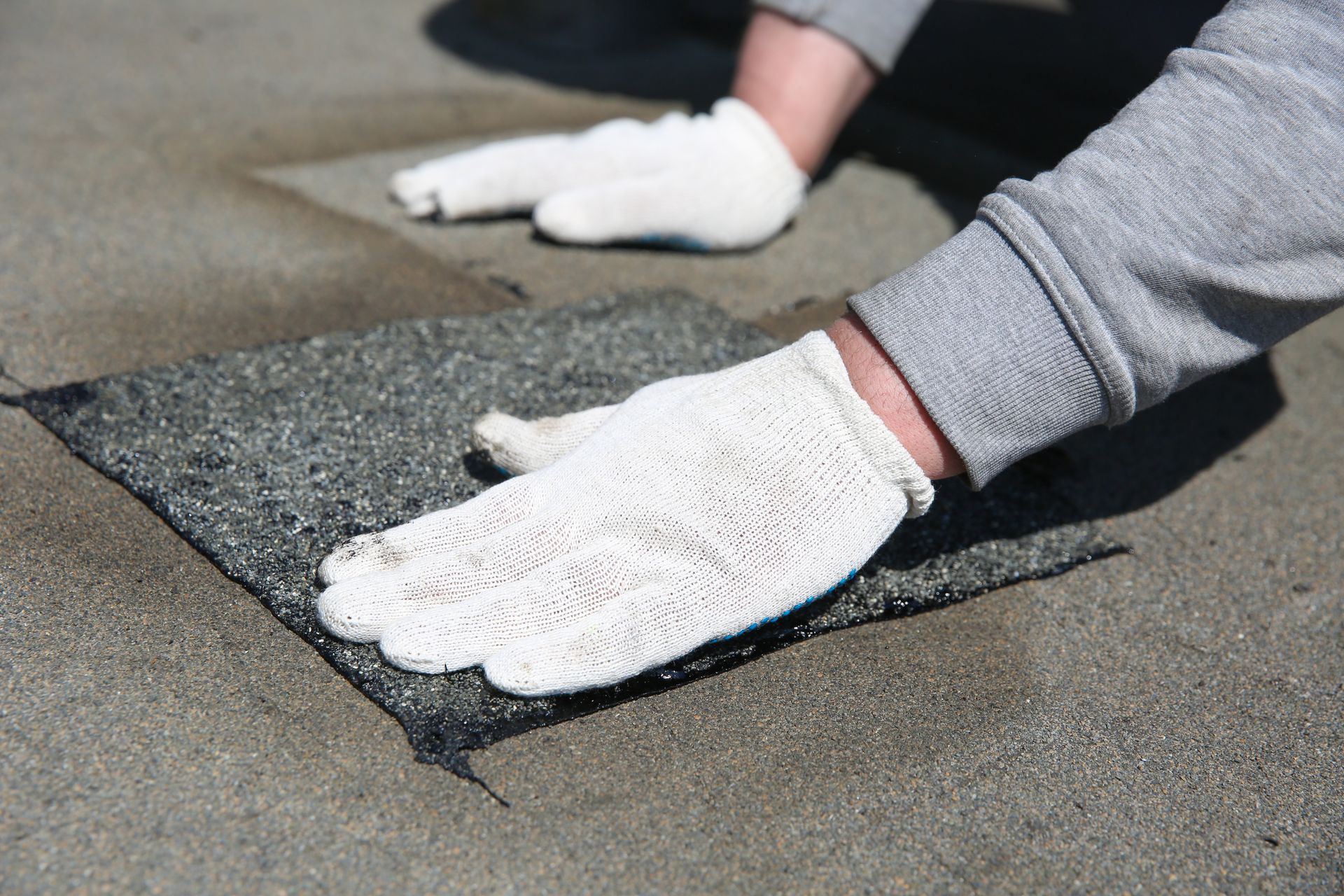 Person wearing gloves applying a dark shingle patch to a roof.