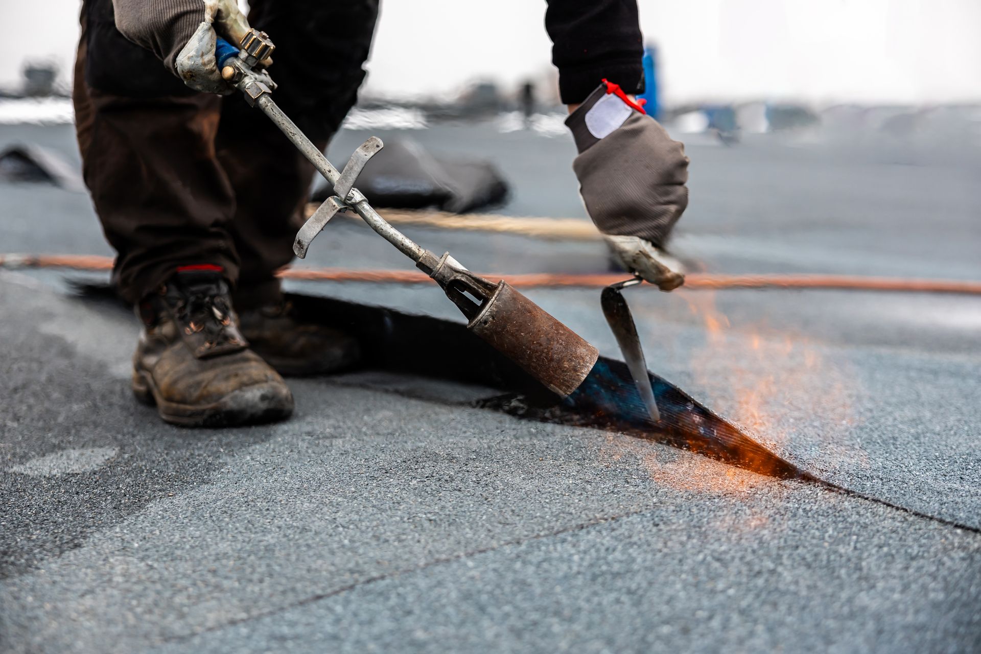 Roofer using a torch to seal a seam on a dark, flat roof. Flames visible.