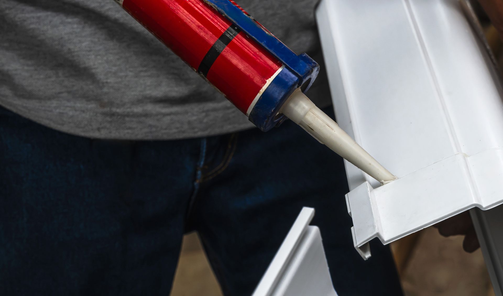 Person applying caulk from a red and blue tube to white molding.