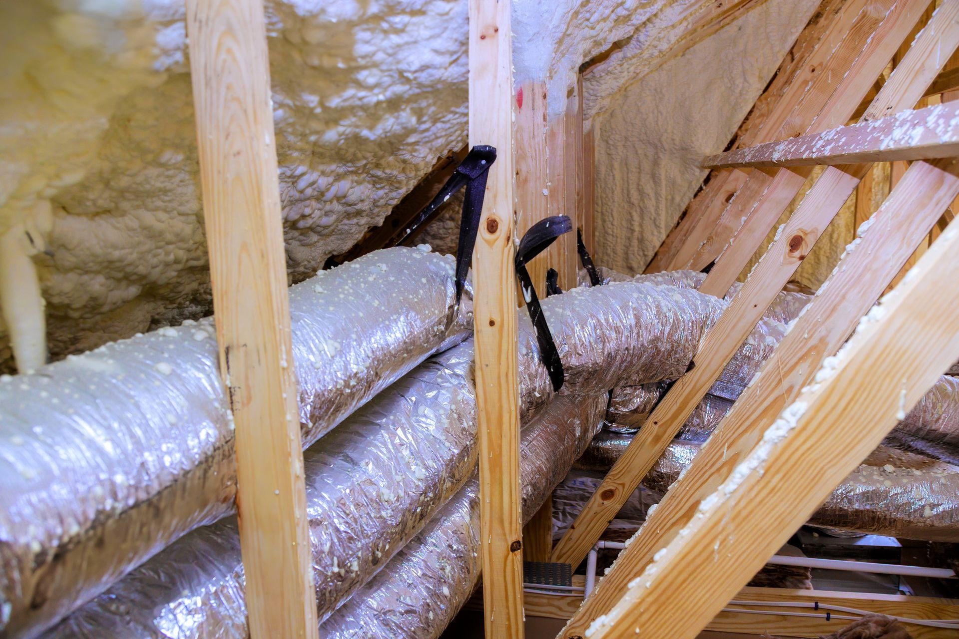 View of an attic with insulated ductwork and wooden rafters.