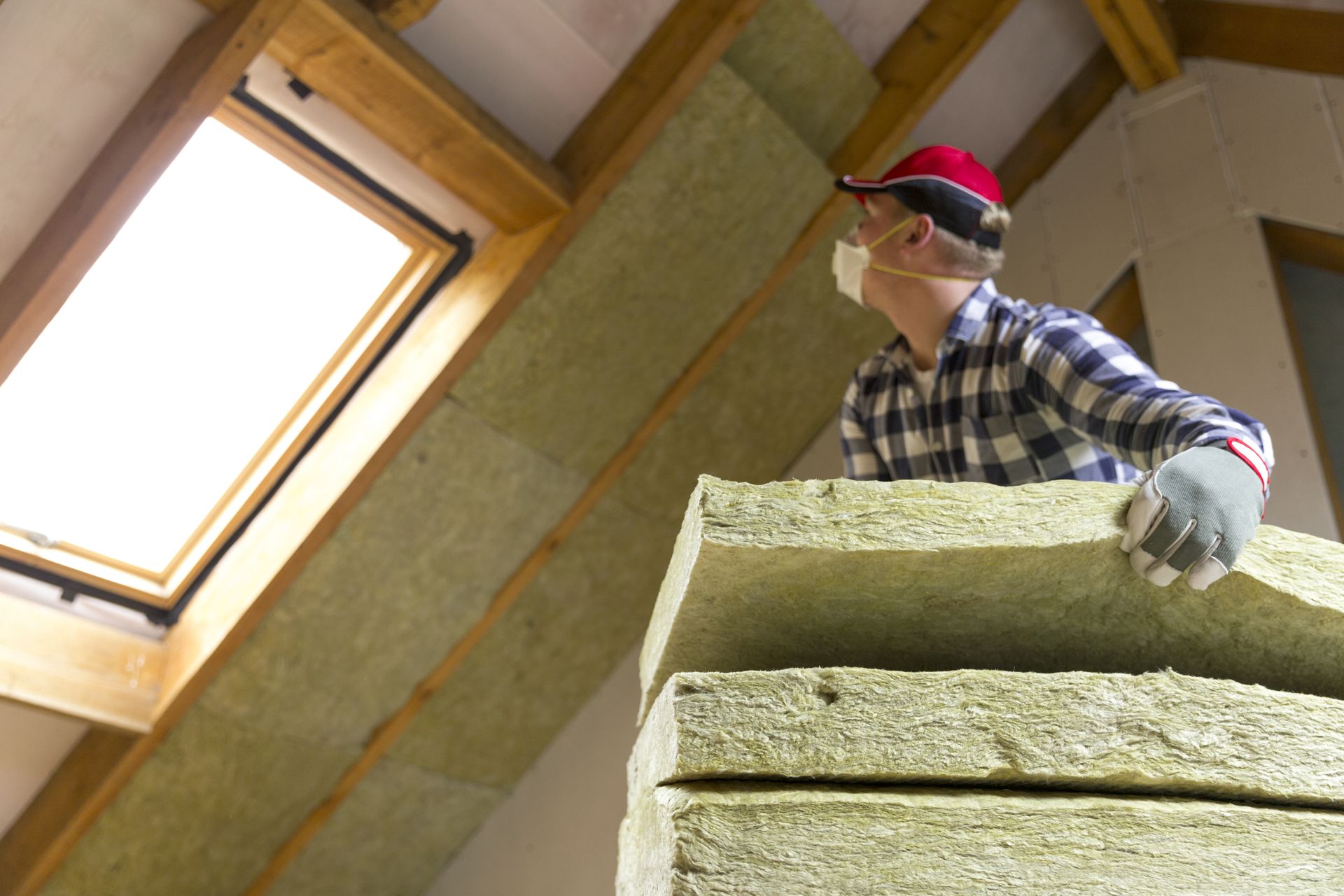 Man installing insulation in an attic, wearing a mask and gloves.