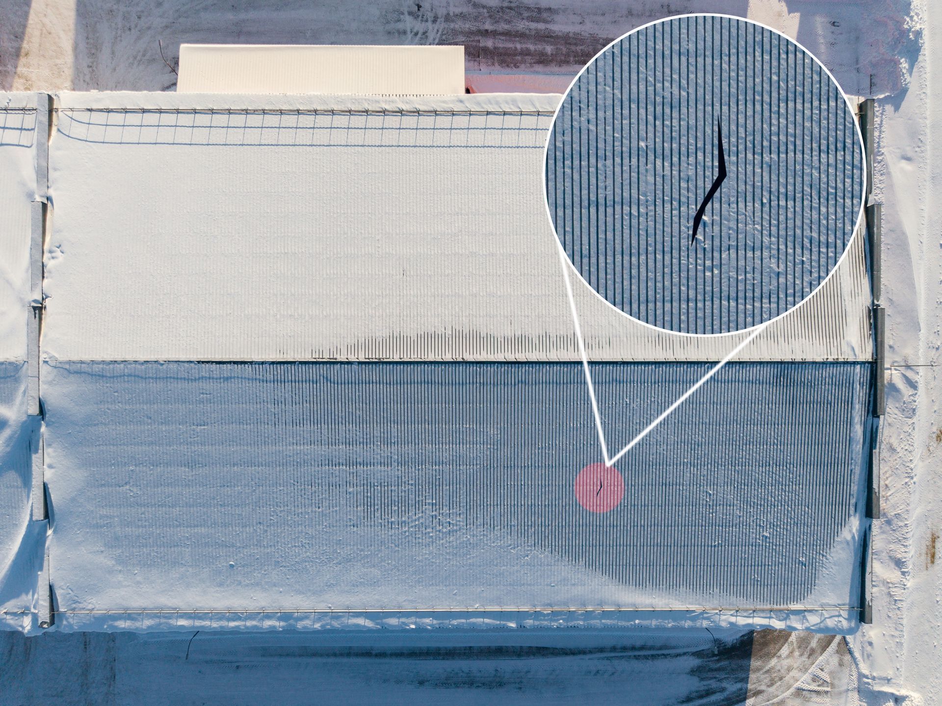 Overhead view of a building with a crack in the blue roof, zoomed in circle highlights the damage.
