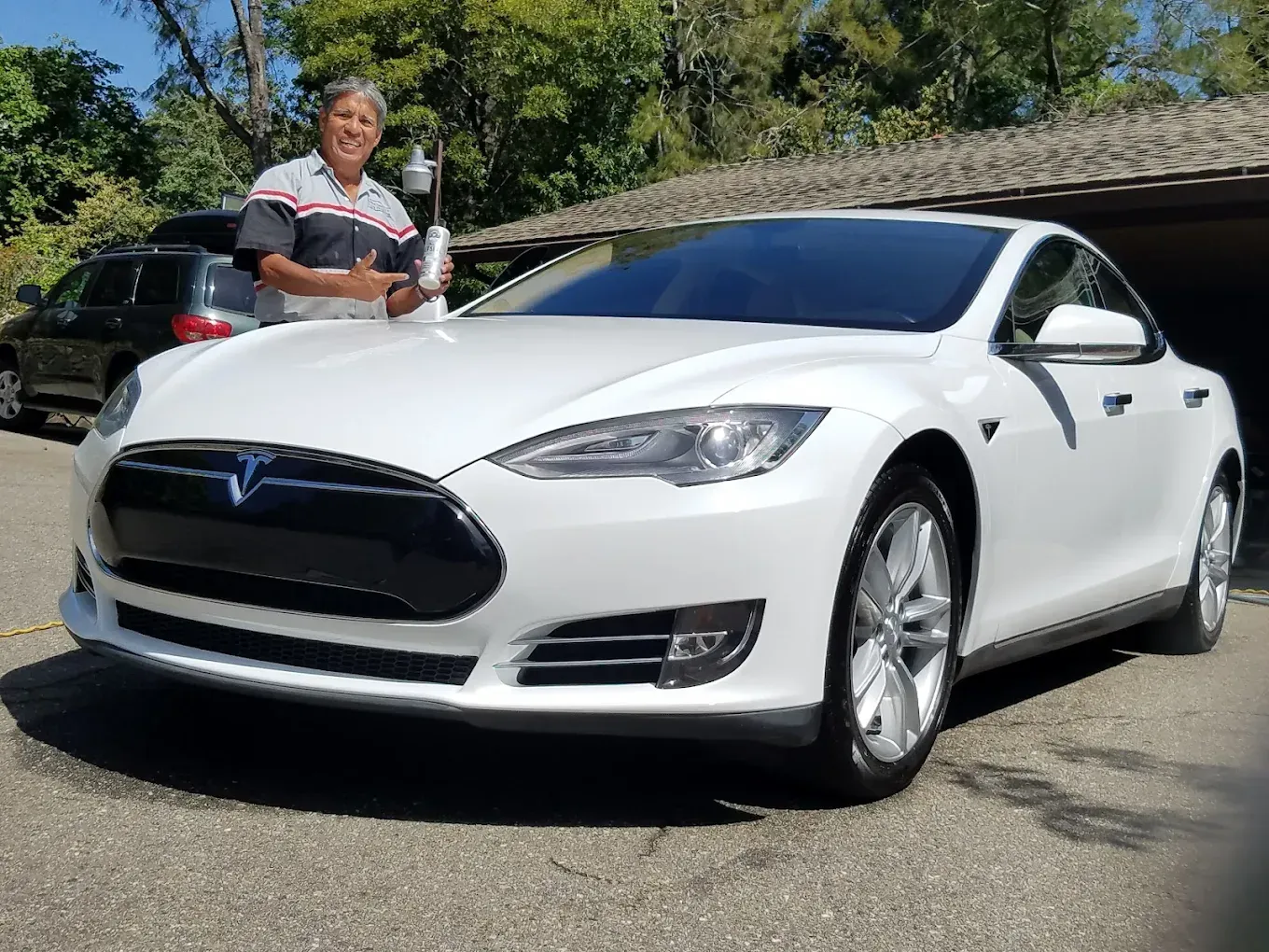 Man holding a bottle next to a white Tesla sedan in a driveway.